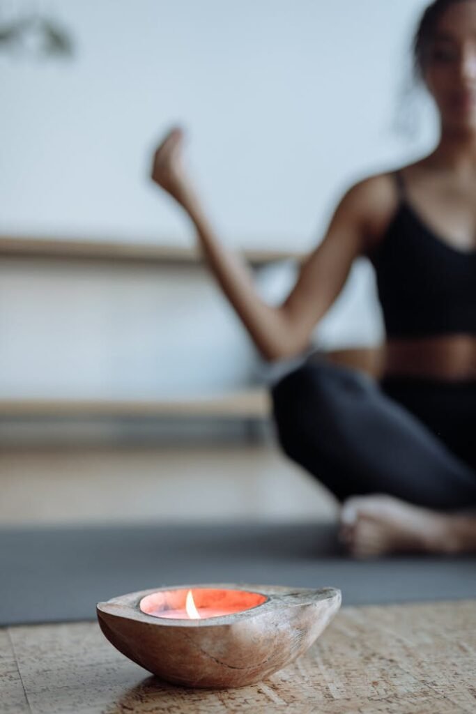 A woman meditates on a yoga mat with a lit candle in focus, creating a calming atmosphere.